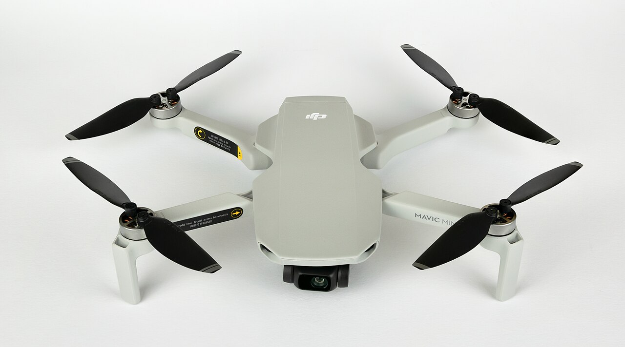 A DJI Mavic Mini camera drone photographed from above on a white background, arms unfolded and camera gimbal visible.